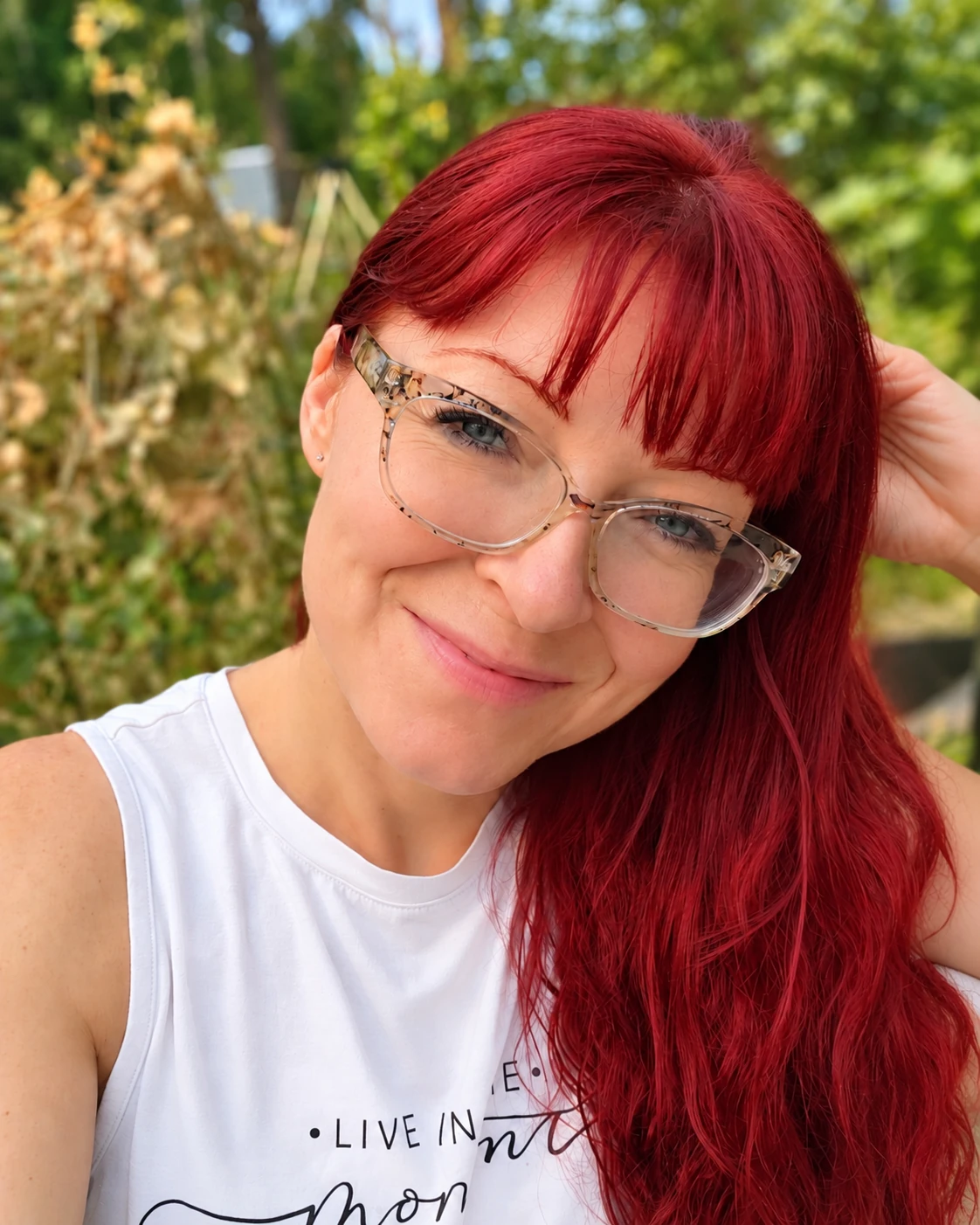 Wendy smiling naturally outside in a white top, with one hand resting in her red hair